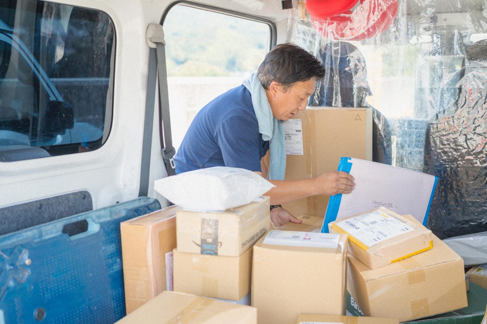 軽貨物車の荷台で段ボールの荷物を仕分ける I さん（40 代男性ドライバー）