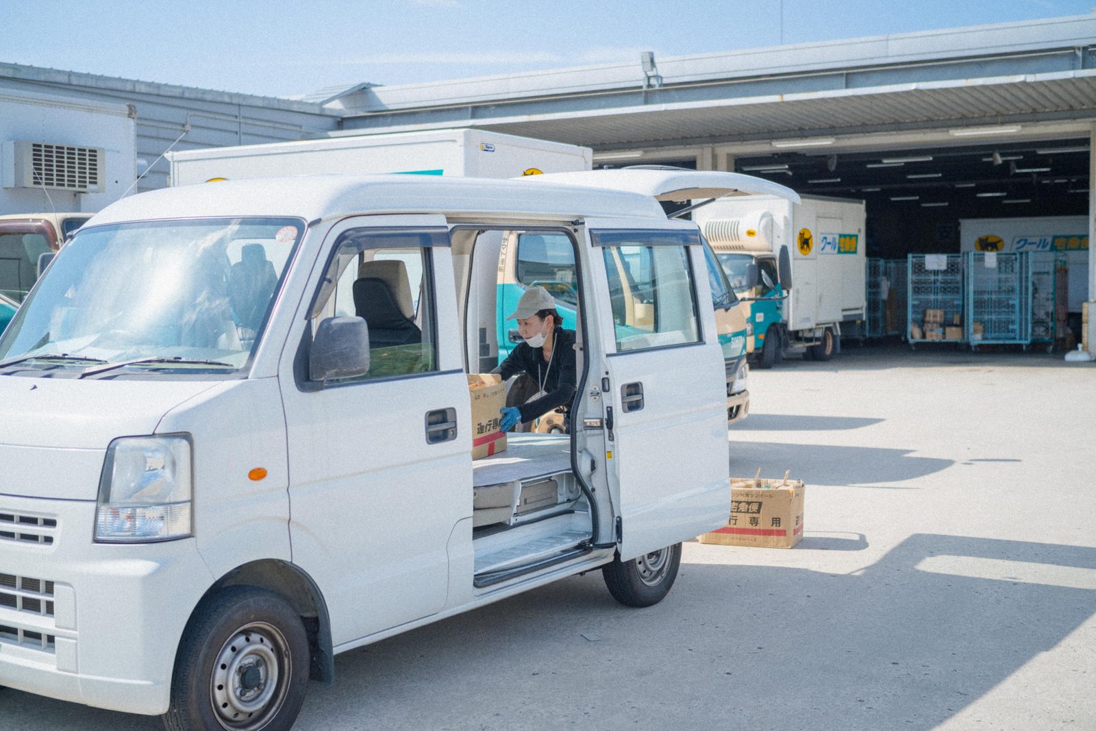 配送センターで軽貨物車の助手席側から段ボールを車内に積み込む O さん